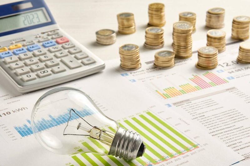 Imagen de una calculadora, monedas de euro, una bombilla y factura de la luz.